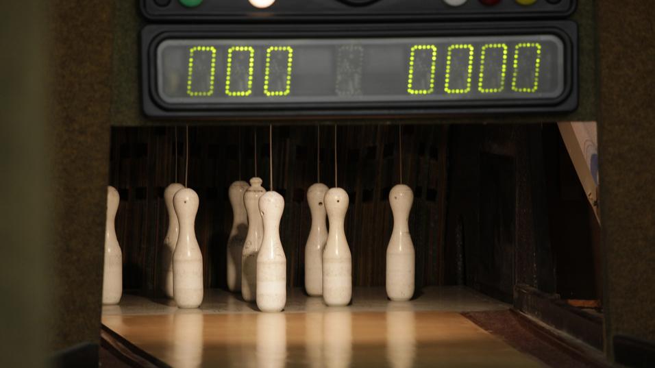 Nahaufnahme von Kegel auf einer Kegelbahn mit einem Punktestand-Anzeigegerät im Hintergrund.